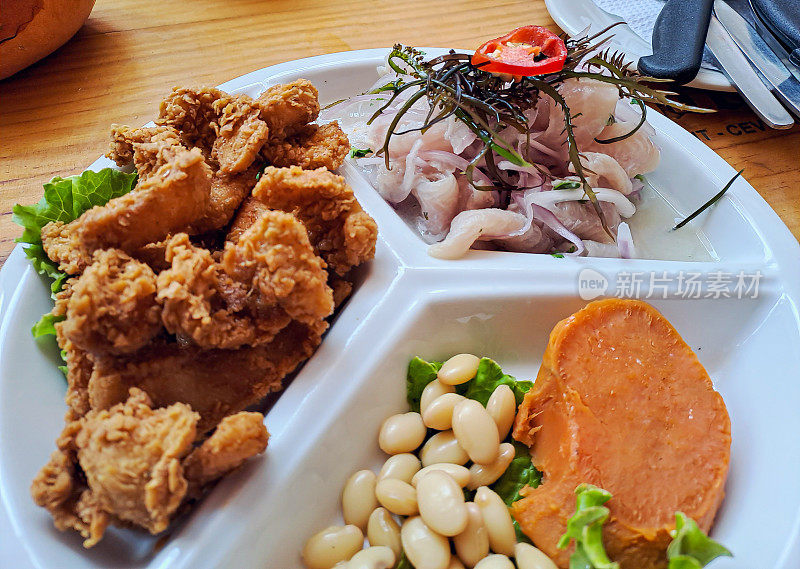 酸橘汁腌鱼，chicharrón de pescado y frijoles con camote, en un plato dividido en 3, sobre una mesa de restaurante。